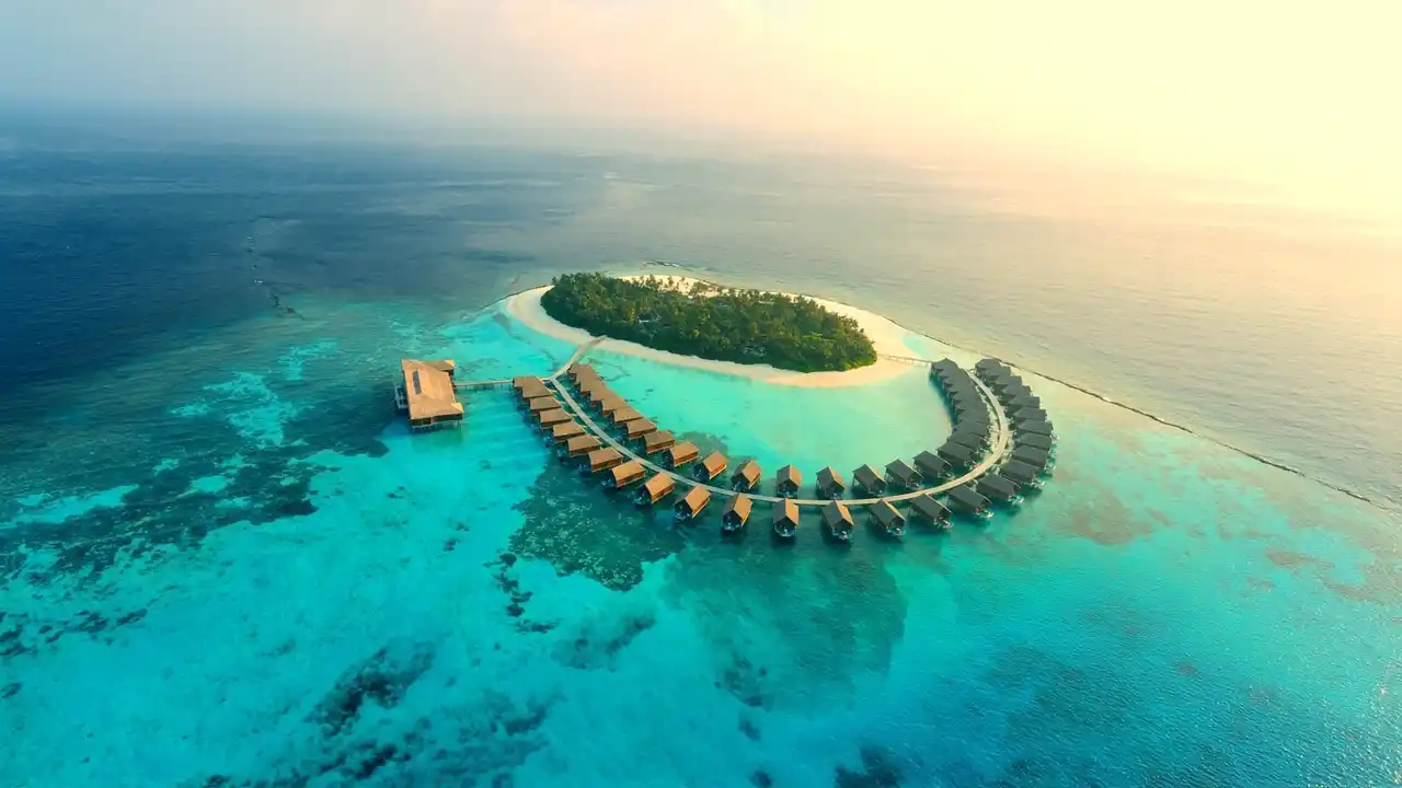 A small island ringed by water villas in the Maldives, at sunrise